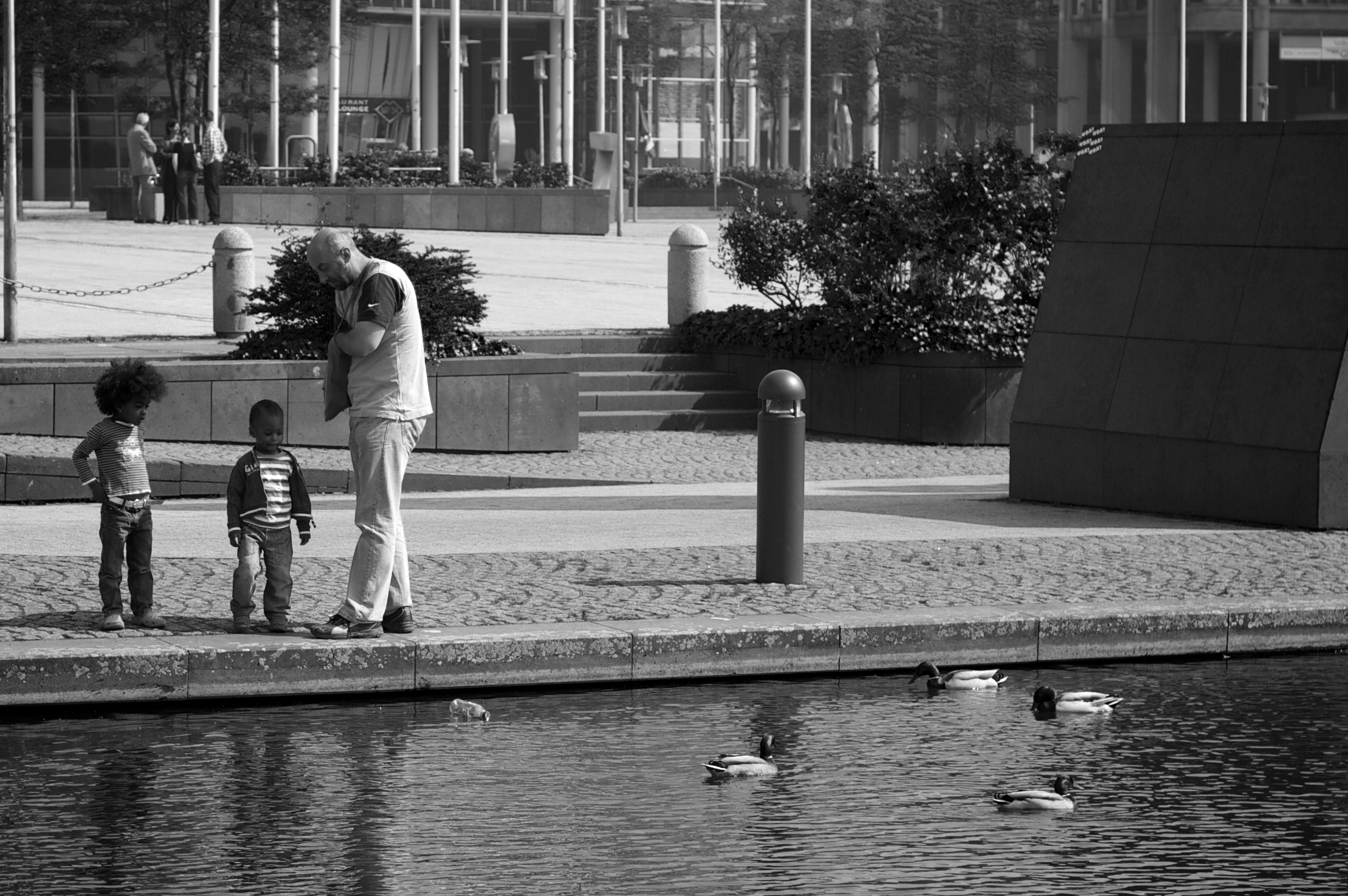 Probably a father with his children, watching and feeding ducks.